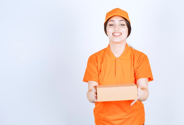 Cheerful young courier holding box on white wall