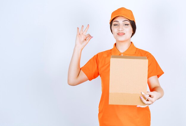 Cheerful young delivery woman on white wall while holding open box
