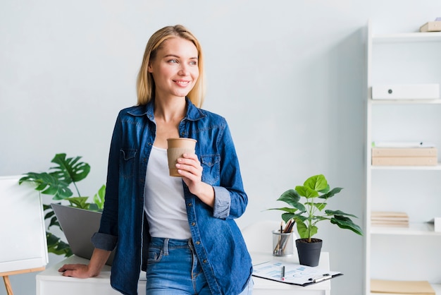 Free photo cheerful young female holding paper cup on break at work