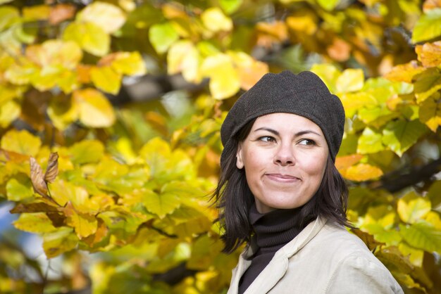 Веселая молодая женщина в шляпе с красивыми желтыми осенними листьями в