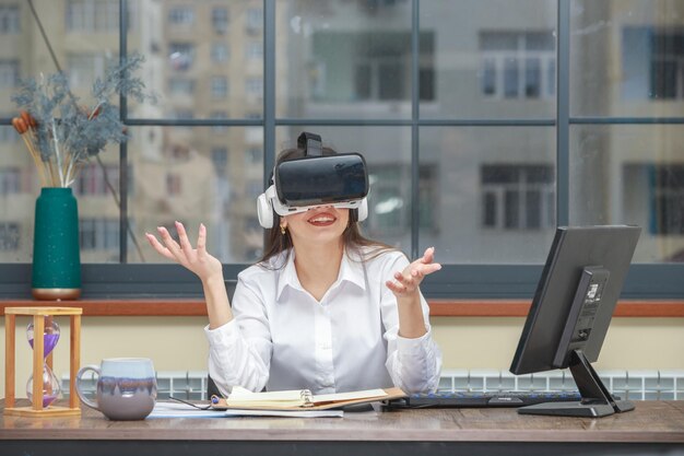 Cheerful young girl wearing VR glasses and smiling at the desk