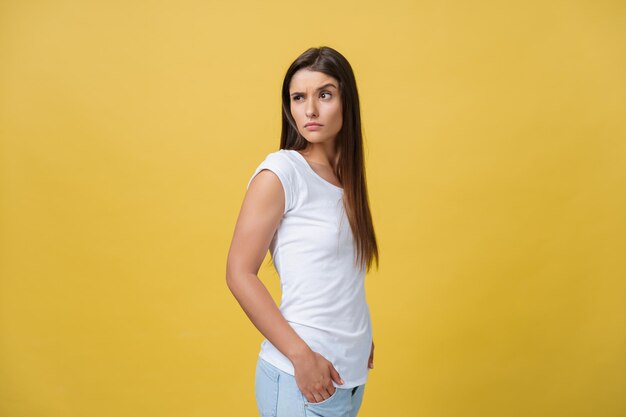 Cheerful young girl winks and look away at the camera in a studio on a yellow background