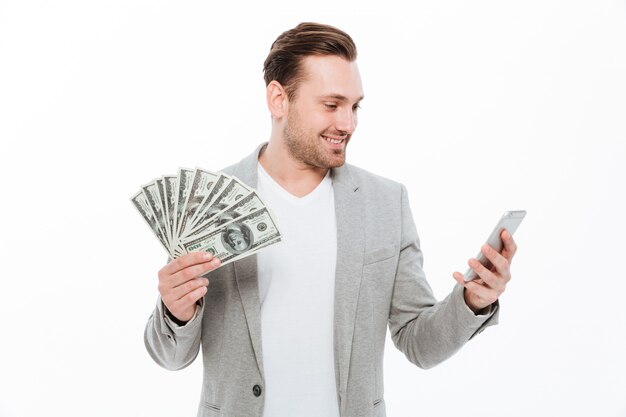 Cheerful young handsome businessman holding money and using mobile phone.