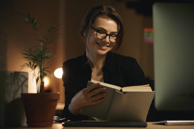 Cheerful young lady designer reading book.