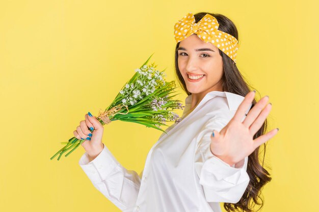 Cheerful young lady holding a bunch of flowers and dancing on yellow background