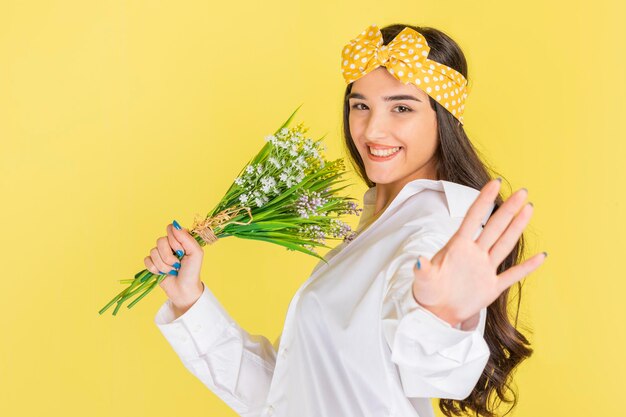 花の束を保持し、黄色の背景で踊る陽気な若い女性