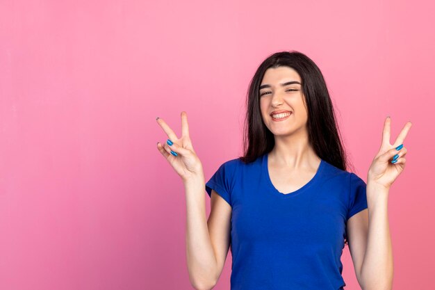 Free photo cheerful young lady holding peace sign with both hands and smiling
