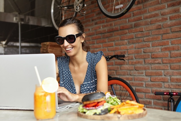 Cheerful young lady in shades sitting in front of laptop computer