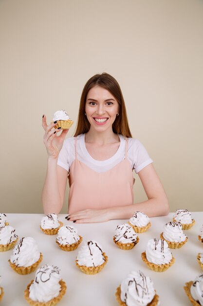 Free photo cheerful young lady sitting and posing near cupcakes on table