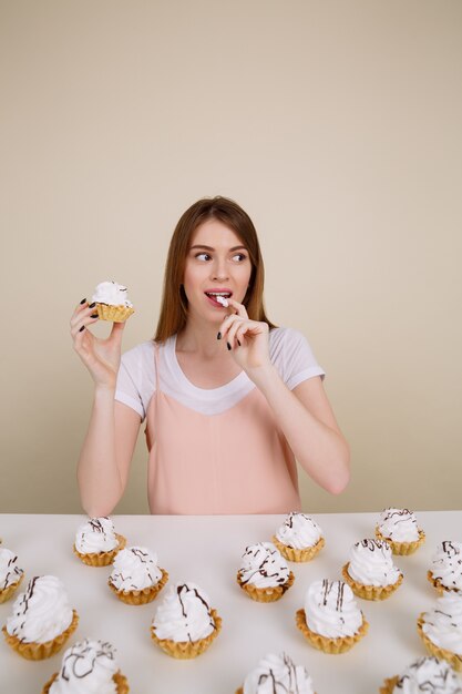 Cheerful young lady sitting and posing while holding cupcake