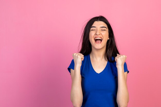 Cheerful young lady squeezing her fists and screaming High quality photo