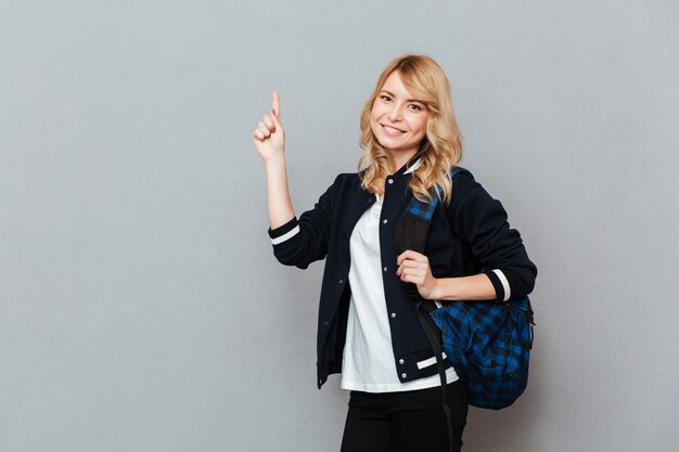 Cheerful young lady student with backpack pointing