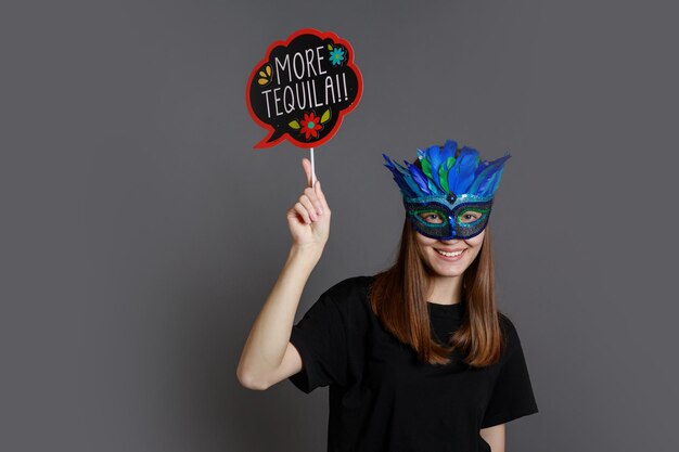 Cheerful young lady wears carnival mask and holding board