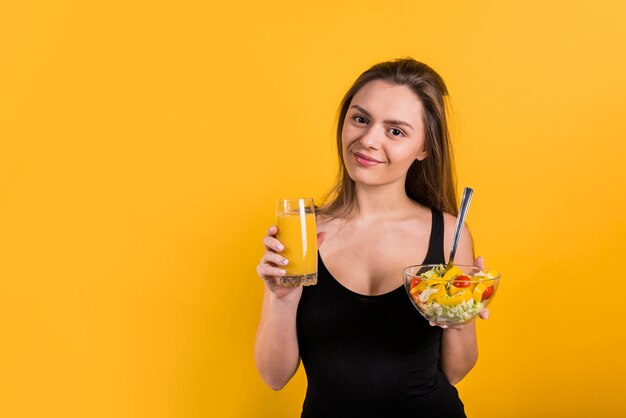 Cheerful young lady with glass of juice and bowl of salad