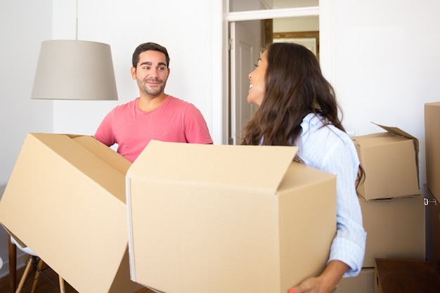 Allegro giovane coppia latina che trasportano scatole di cartone nel loro nuovo appartamento, parlando e ridendo
