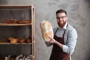 無料写真 陽気な若い男のパン屋のパンを保持しているベーカリーに立っています。