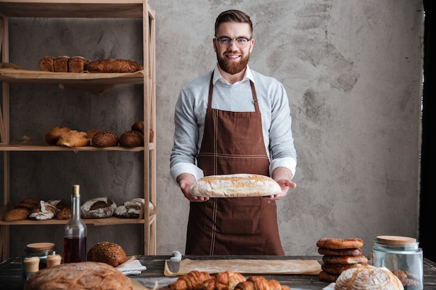 Free photo cheerful young man baker standing at bakery holding bread