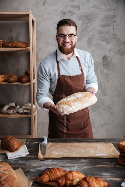 빵을 들고 빵집에 서있는 쾌활한 젊은 남자 베이커
