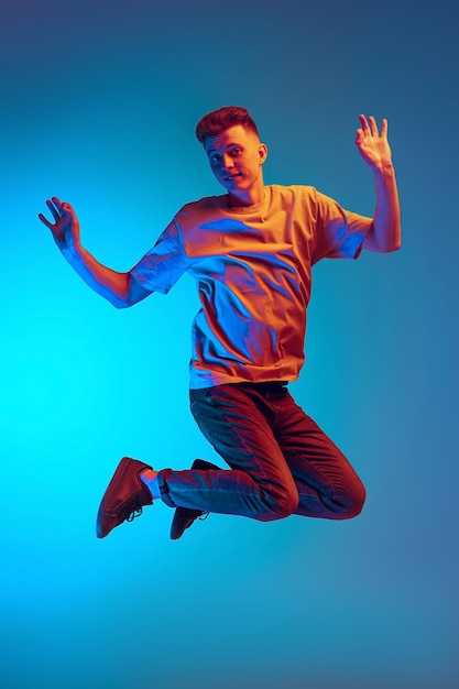 Cheerful young man in casual cloth jumping posing isolated over blue background in neon