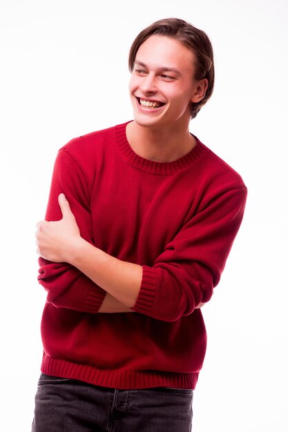 Cheerful young man holding hands in pockets and looking at front while standing against white wall