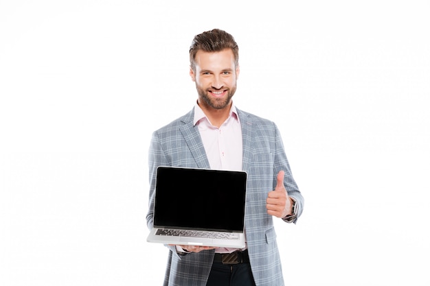 Cheerful young man holding laptop showing thumbs up.