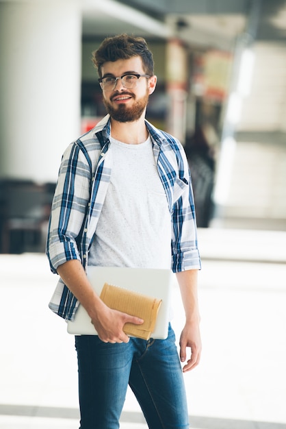 陽気な若い男のノートとラップトップを保持していると横向き