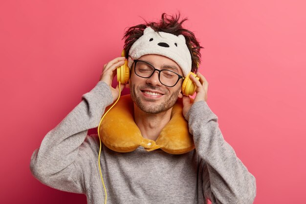 Cheerful young man listens music via headphones, smiles pleasantly