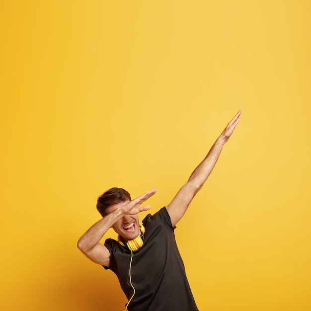 Free photo cheerful young man makes dab dance gesture, shows dabbing movement