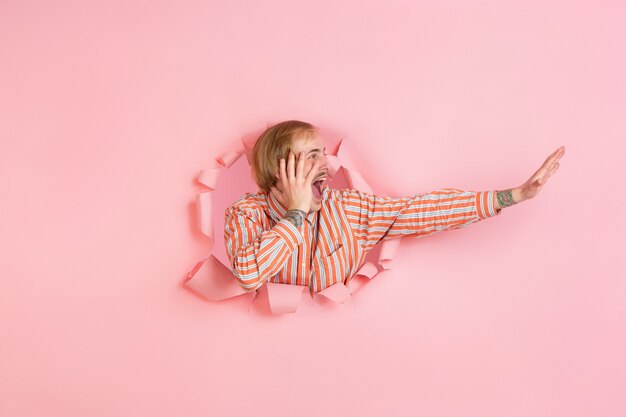 Cheerful young man poses in torn coral paper hole, emotional and expressive