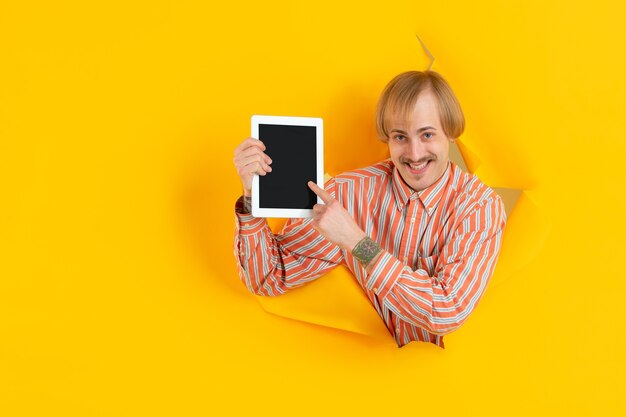 Cheerful young man poses in torn yellow paper hole wall emotional and expressive