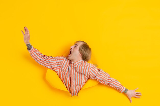 Cheerful young man poses in torn yellow paper hole wall emotional and expressive