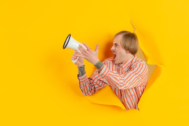 Веселый молодой человек позирует в рваной желтой стене с отверстиями для бумаги эмоционально и выразительно