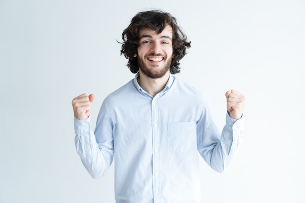 Cheerful young man pumping fists and looking at camera