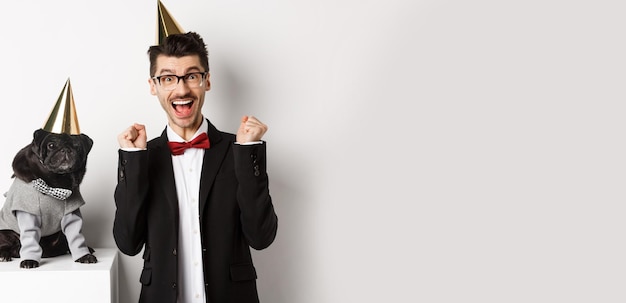 Cheerful young man shouting for joy dog and owner wearing birthday party cones and celebrating guy r