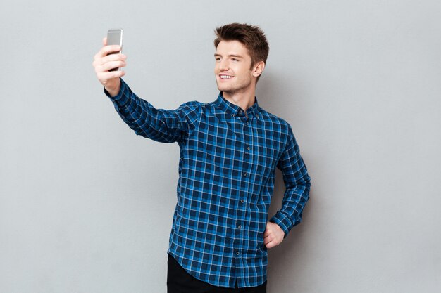 Cheerful young man standing over grey wall and make selfie