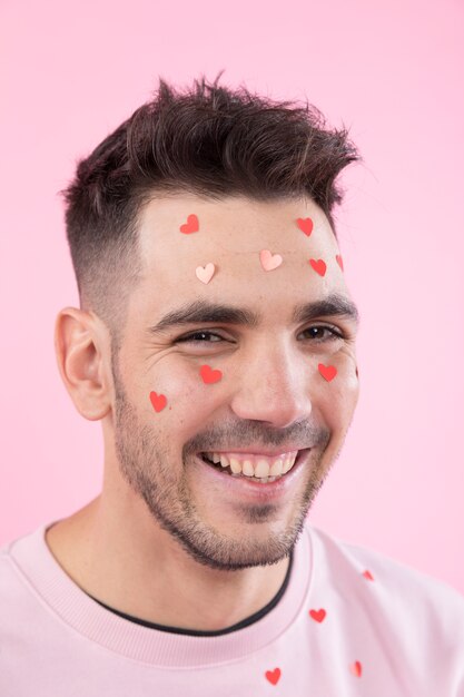Веселый молодой человек с бумажными сердечками на лице