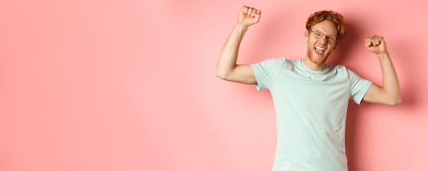 Free photo cheerful young man with red hair looking happy raising hands up in fist pumps gesture celebrating su