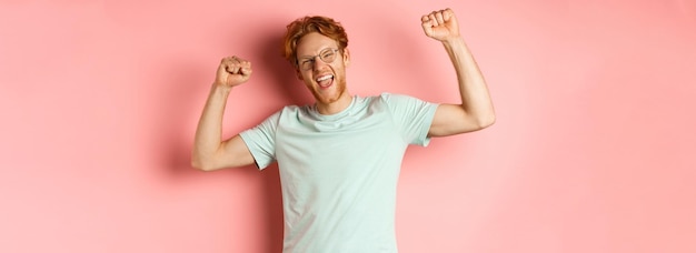 Free photo cheerful young man with red hair looking happy raising hands up in fist pumps gesture celebrating su