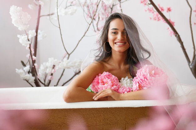 꽃 다발과 함께 욕조에 앉아 있는 쾌활한 젊은 모델 고품질 사진