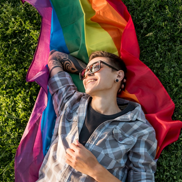 Cheerful young person lying on LGBT flag in park