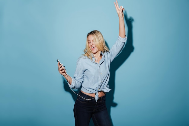 Cheerful young pretty blonde woman listening music with earphones.