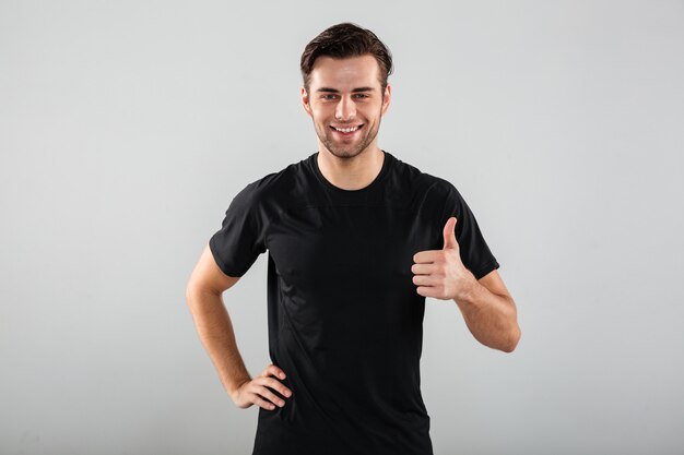 Cheerful young sports man posing showing thumbs up gesture.