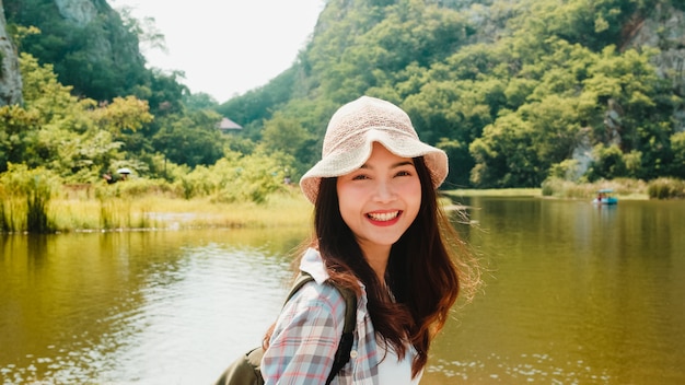 山の湖で歩いてバックパックで陽気な若い旅行者のアジアの女性。韓国の十代の少女は幸せな自由を感じて彼女の休暇の冒険をお楽しみください。ライフスタイルは旅行し、自由な時間の概念でリラックスします。
