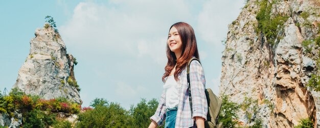 Cheerful young traveler Asian lady with backpack walking at the mountain lake. Korean teen girl enjoy her holidays adventure feeling happy freedom. Lifestyle travel and relax in free time concept.
