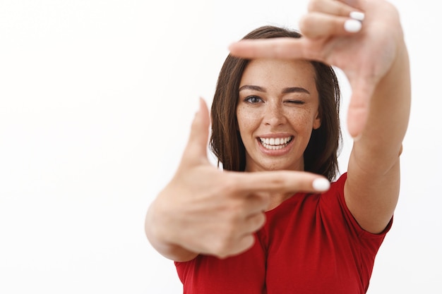 Cheerful young upbeat woman feeling lucky searching perfect angle, making finger frames and looking through playfully winking, smiling happily