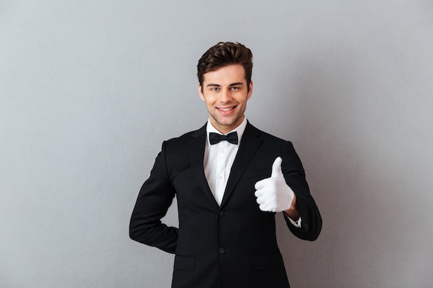 Free photo cheerful young waiter standing isolated showing thumbs up.