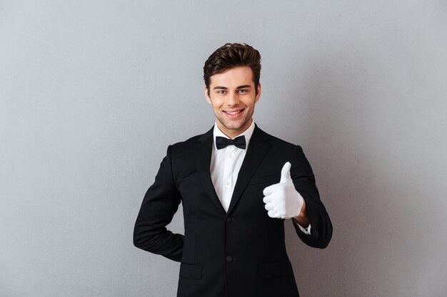 Cheerful young waiter standing isolated showing thumbs up.