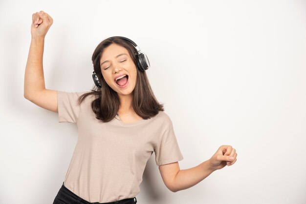 Cheerful young woman in beige shirt dancing and listening music in headphones.