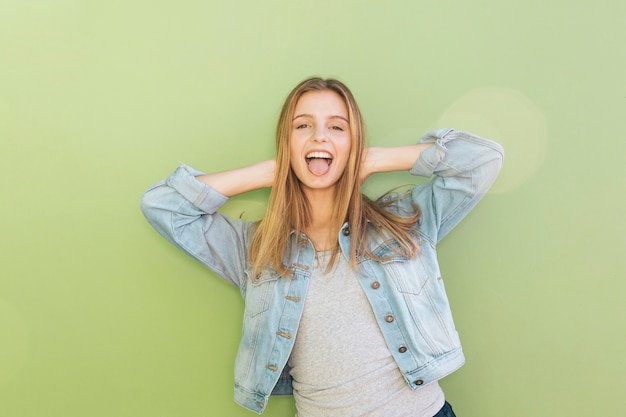 Free photo cheerful young woman in blue jacket with her hands behind head against green backdrop