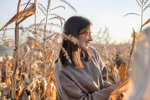 Веселая молодая женщина на кукурузном поле осенью.